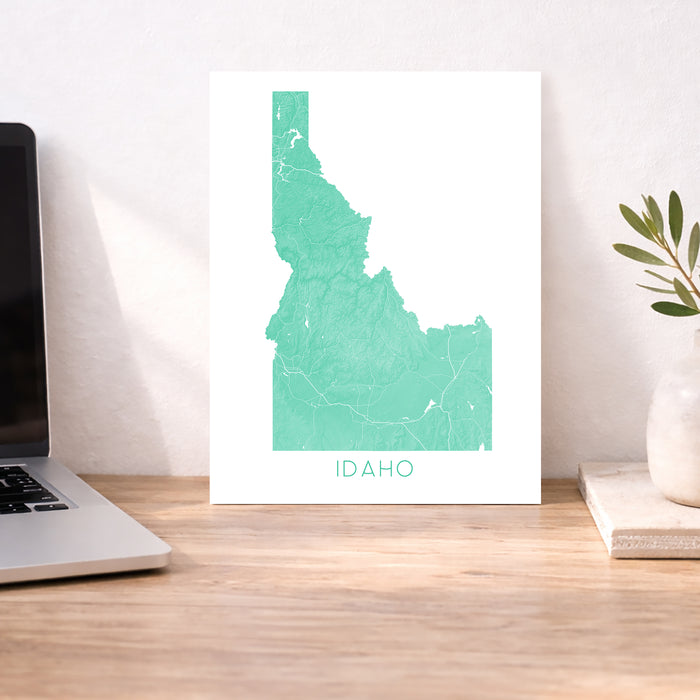 Map of Idaho on a white wall above a desk with a laptop and plant.