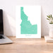 Map of Idaho on a white wall above a desk with a laptop and plant.