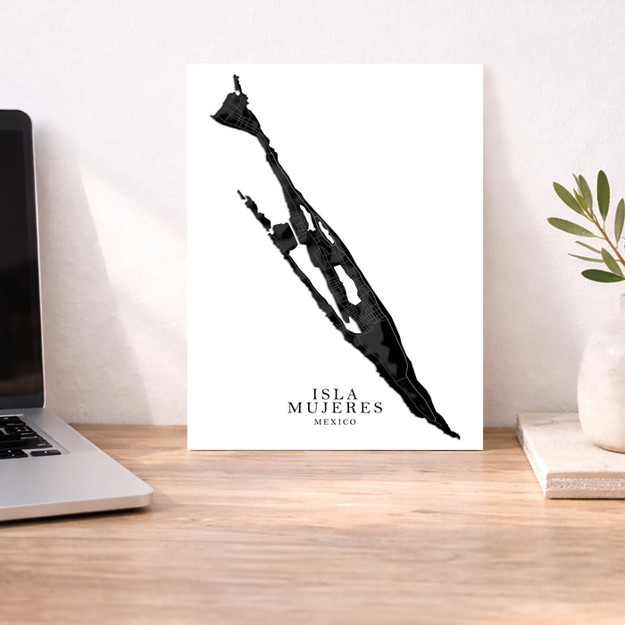 Poster of a silhouette with 'Isla Mujeres, Mexico' text on a desk with a laptop and plant.