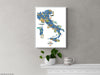 Framed map of Italy on a gray wall with a plant and mug below.