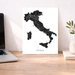 Map of Italy on a white background next to a laptop on a wooden desk.