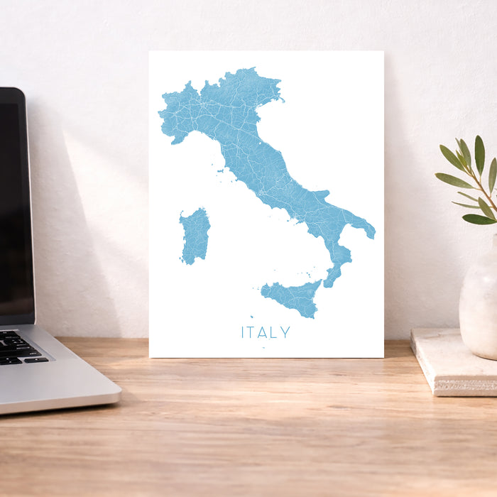 Map of Italy on a desk with a laptop and plant