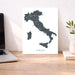 Map of Italy on a white background next to a laptop on a wooden desk.