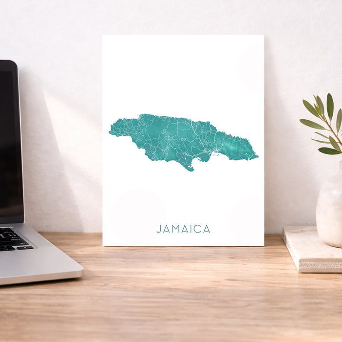 Map of Jamaica on a white background next to a laptop on a wooden desk.