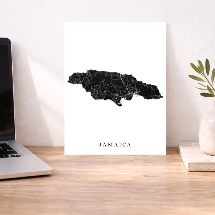 Map of Jamaica on a white background next to a laptop on a wooden desk.