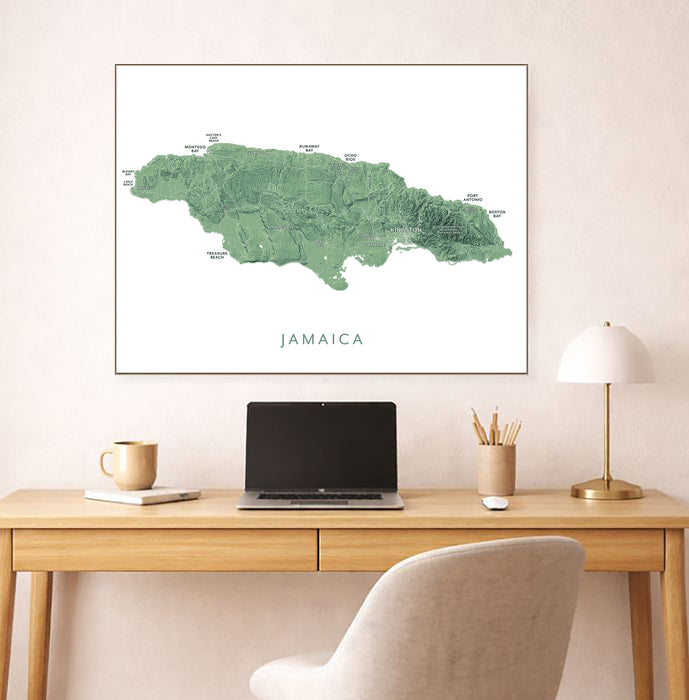 Framed map of Jamaica on a wall above a desk with a laptop and lamp.