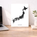 Map of Japan on a white background next to a laptop on a wooden desk.