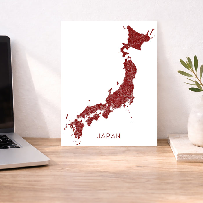 Map of Japan on a white background next to a laptop on a wooden desk.