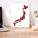 Map of Japan on a white background next to a laptop on a wooden desk.