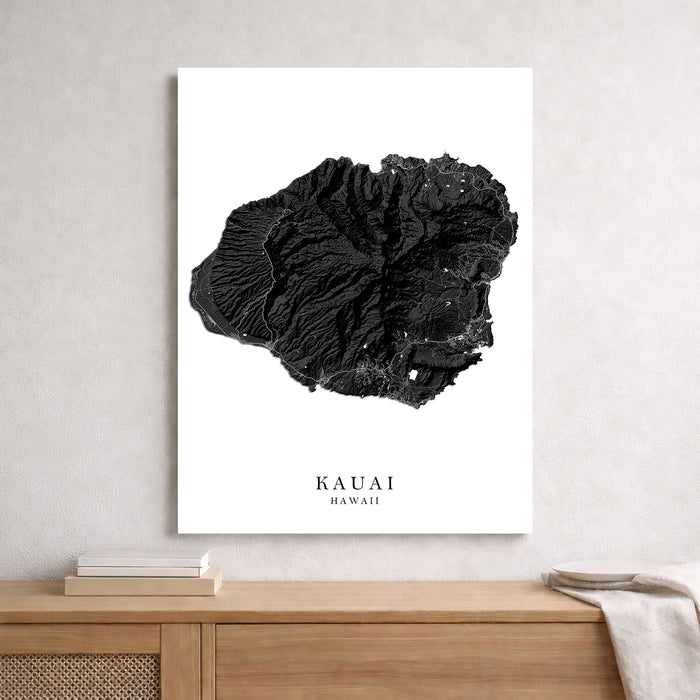 Black and white map of Kauai, Hawaii on a white wall above a wooden shelf.
