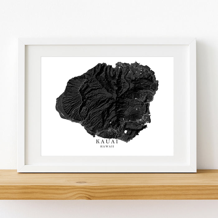 Framed black and white topographic map of Kauai, Hawaii on a wooden shelf.