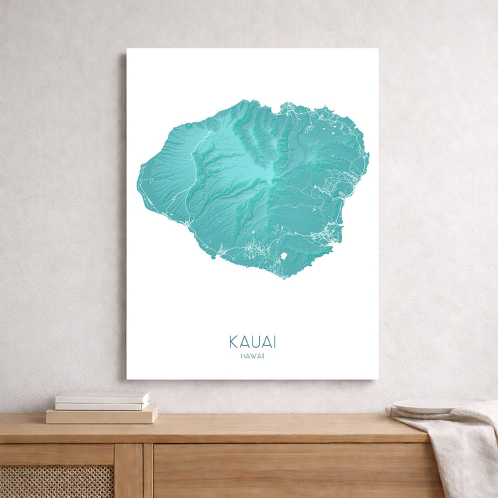 Teal topographic map of Kauai on a white background, framed and leaning against a light gray wall.