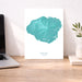 Teal map of Kauai on a white background, displayed on a wooden desk with a laptop and plant.