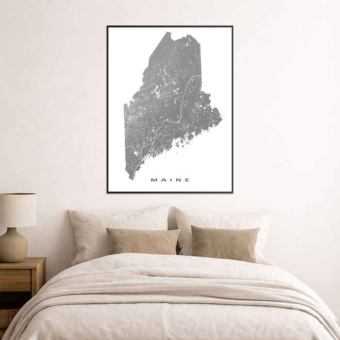 Framed map of Maine on a wall above a bed in a bedroom.