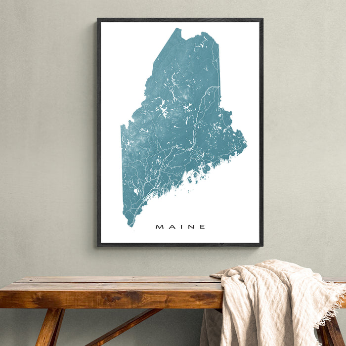 Framed map of Maine on a wall above a wooden bench.