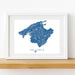 Framed map of Mallorca with blue and white design on a wooden shelf.