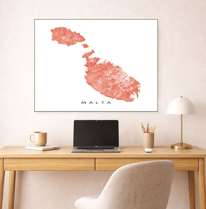 Framed map of Malta on a wall above a desk with a laptop and office items.