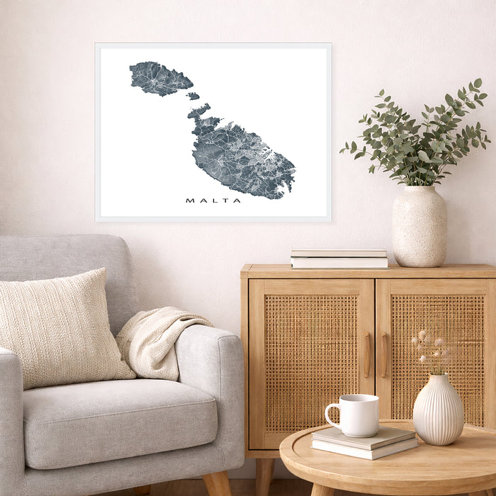 Living room with a map of Malta on the wall, a couch, and a side table with a vase and books.