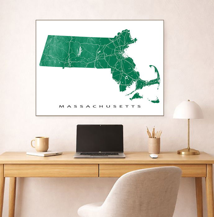 Framed map of Massachusetts on a wall above a desk with a laptop and lamp.