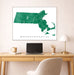 Framed map of Massachusetts on a wall above a desk with a laptop and lamp.