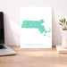Map of Massachusetts on a white background next to a laptop on a wooden desk.