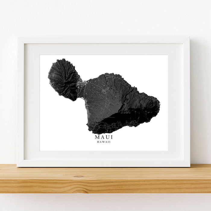 Framed black and white map of Maui, Hawaii on a wooden shelf.