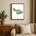 Framed green map of Maui on a wall above a beige sofa with a plant beside it.