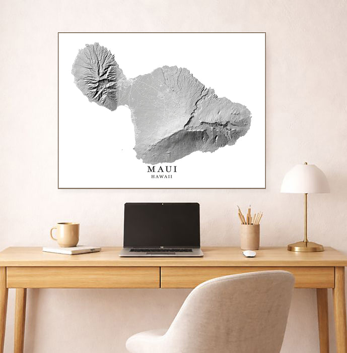Framed map of Maui, Hawaii above a desk with a laptop and lamp.