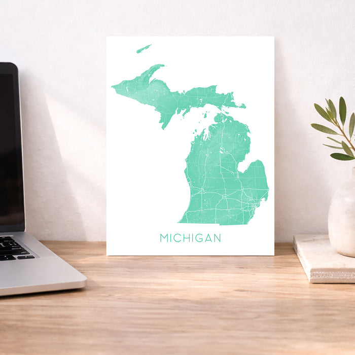 Map of Michigan on a white background next to a laptop on a wooden desk.