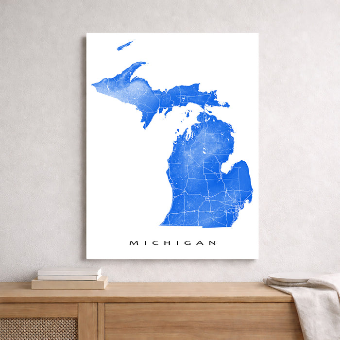 Map of Michigan in blue on a white background, framed and hanging on a wall above a wooden surface.