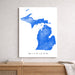 Map of Michigan in blue on a white background, framed and hanging on a wall above a wooden surface.