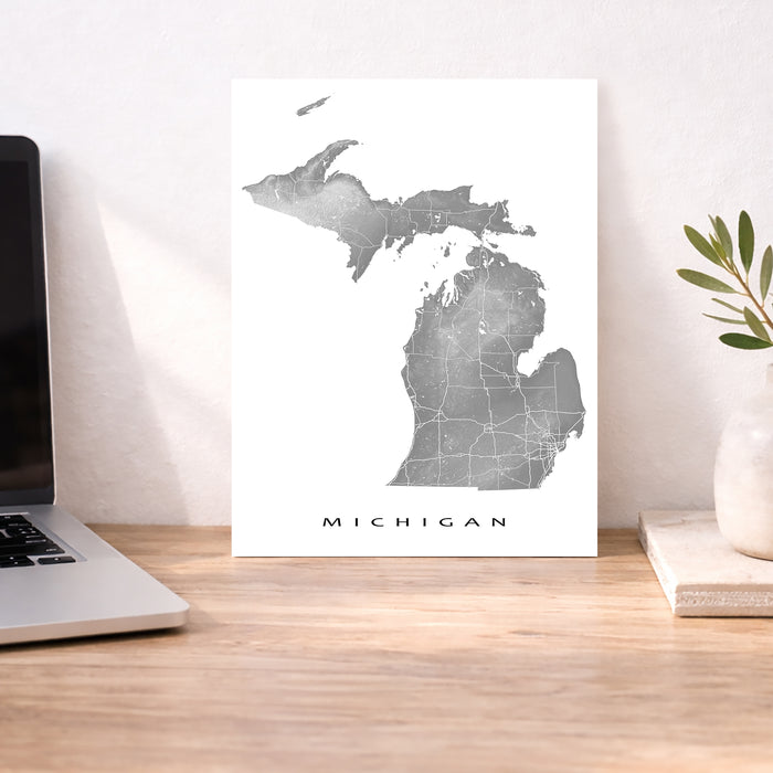 Map of Michigan on a white background next to a laptop on a wooden desk.