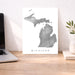 Map of Michigan on a white background next to a laptop on a wooden desk.