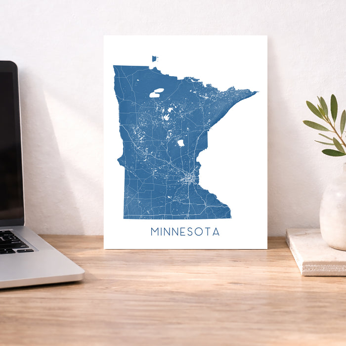 Map of Minnesota on a white background next to a laptop on a wooden desk.