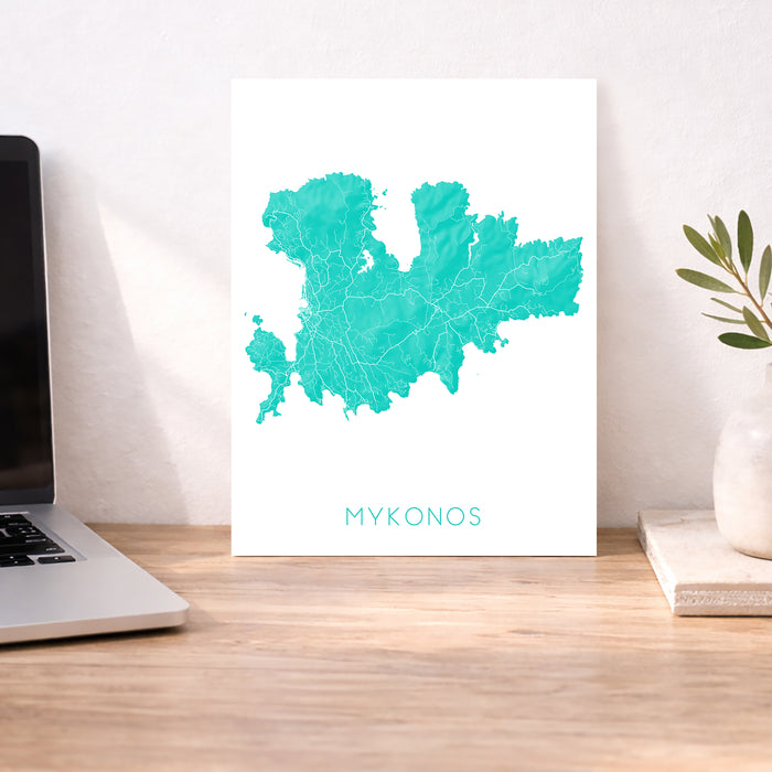 Map of Mykonos on a white background next to a laptop on a wooden desk.