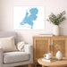 Living room with a map of the Netherlands on the wall, a gray sofa, wooden cabinet, and small table.
