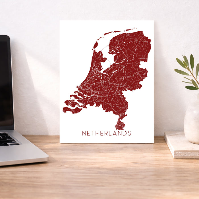 Map of the Netherlands on a white background next to a laptop on a wooden desk.