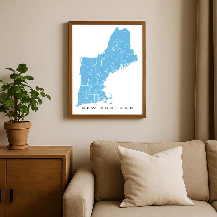 Framed map of New England on a wall above a beige sofa with a plant beside it.