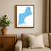 Framed map of New England on a wall above a beige sofa with a plant beside it.