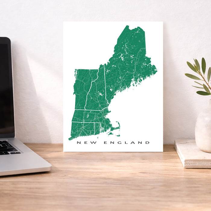 Map of New England on a white background next to a laptop on a wooden desk.