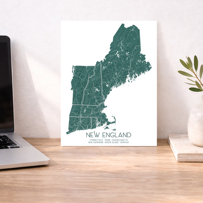 Map of New England on a desk with a laptop and plant