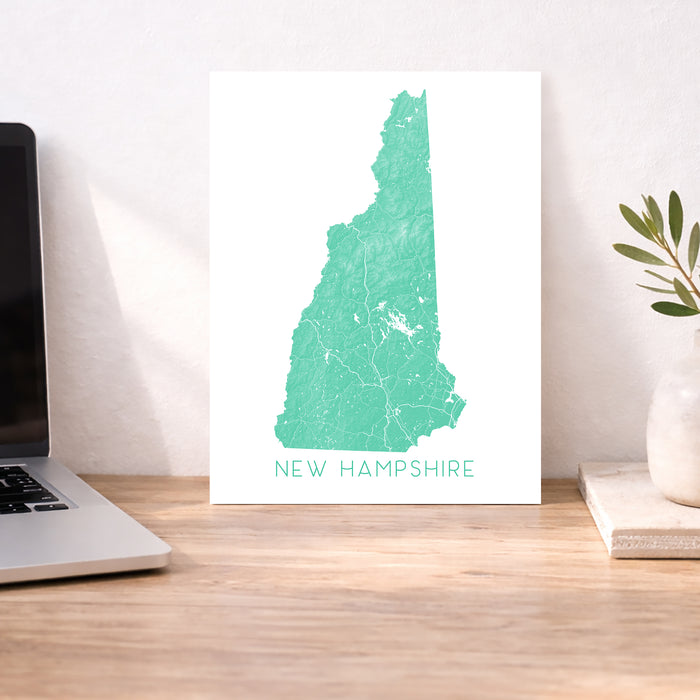 Map of New Hampshire on a desk with a laptop and plant