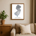Framed map of New Jersey on a wall above a beige sofa with a plant beside it.