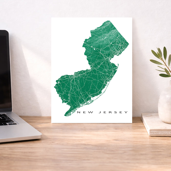 Map of New Jersey on a white background next to a laptop on a wooden desk.