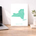 Map of New York on a white background next to a laptop on a wooden desk.