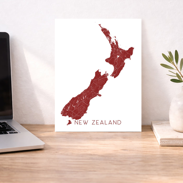 Map of New Zealand on a white background next to a laptop on a wooden desk.