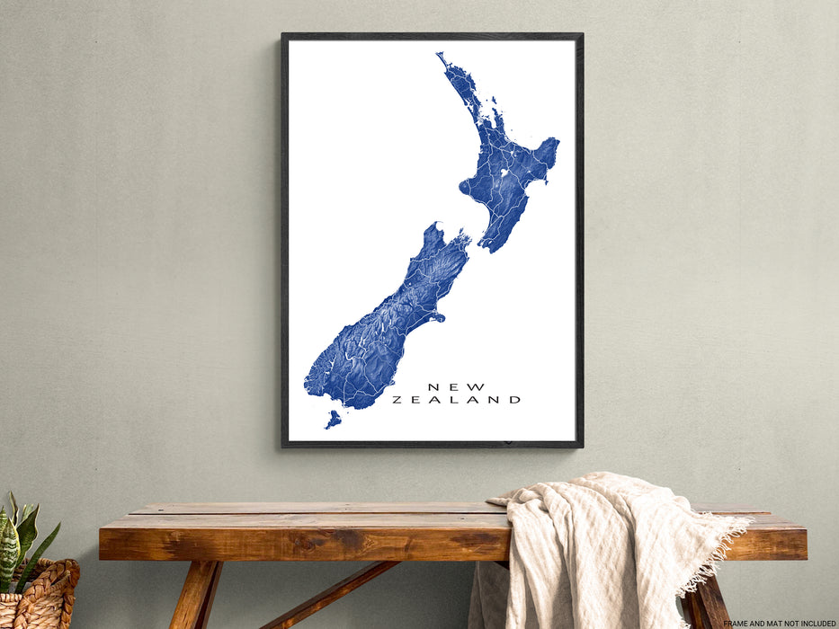 Framed map of New Zealand on a wall above a wooden table.