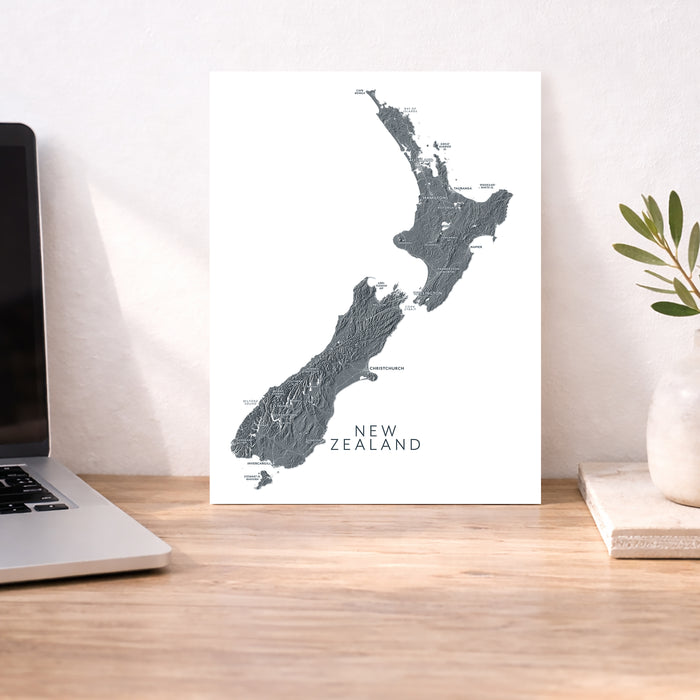 Map of New Zealand on a white background next to a laptop on a wooden desk.