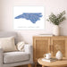 Framed map of North Carolina in a living room setting with a couch, cabinet, and decorative items.