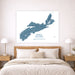 A large square wall art print showing a blue map of Nova Scotia with coordinates and a small compass rose, displayed above a neatly made bed in a bright, modern bedroom.